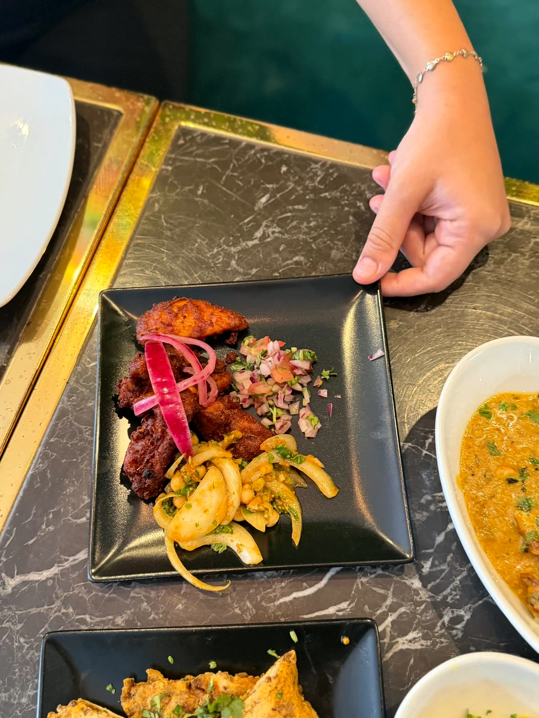 A member of the team setting down a black plate of spiced fried pieces, pickled red onion and chopped salad on a marble table